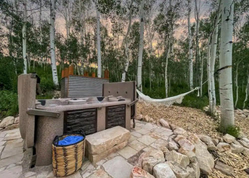 A serene outdoor space featuring a hot tub, hammock, and surrounded by tall trees at sunset.